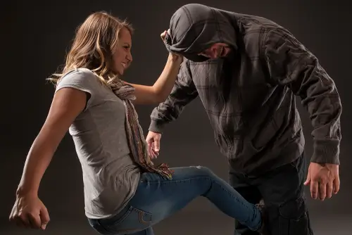 Kampfkunstschule Korean Fighters Werl - Frauen Selbstverteidigung - Kachel Korean Fighters Werl – Frauen-Selbstverteidigung: Frau kontrolliert den Angreifer an der Kapuze, setzt einen tiefen Kick gegen Bein/Knie und schafft Abstand in einer realistischen Übungsszene.