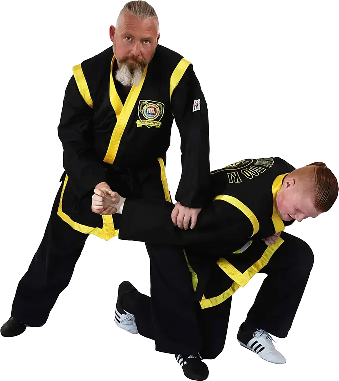 Kampfkunstschule Korean-Fighters Werl - Grossmeister Matthias Michaelis demonstriert Grifftechniken mit Trainingspartner Trainingsfoto bei Korean Fighters Werl: Großmeister Matthias Michaelis demonstriert Griff- und Kontrolltechniken an einem Trainingspartner, der in tiefer Stellung/kniend positioniert ist. Der Großmeister hält den Arm kontrolliert und zeigt Hebel- bzw. Fixierprinzipien – Studioaufnahme auf neutralem Hintergrund.