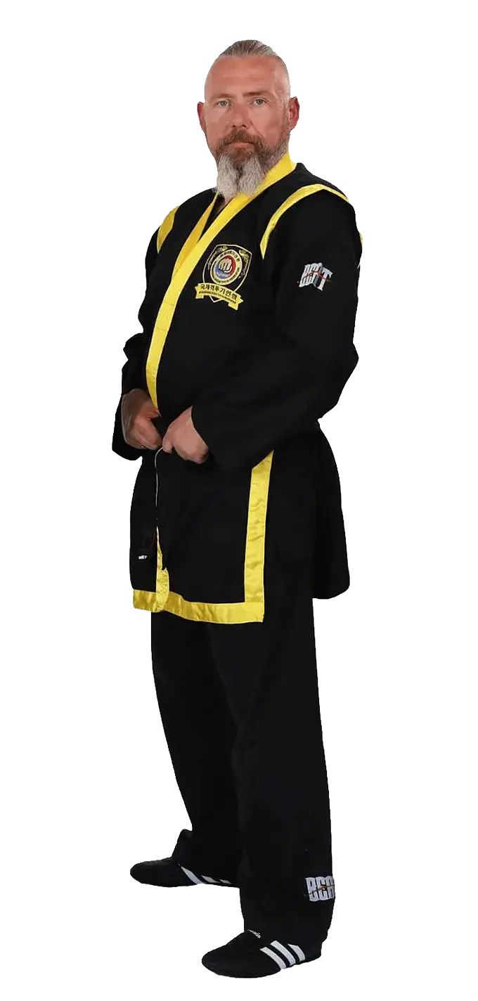 Kampfkunstschule Korean Fighters Werl - Grossmeister Matthias Michaelis im Kampfanzug bestehend aus Dobog sang-ui - Dobog baji und Dobog tti Porträt von Großmeister Matthias Michaelis in schwarzem Dobok (Dobog sang-ui, Dobog baji) mit gelben Akzenten und Dobog tti (Gürtel). Er steht frontal in ruhiger Haltung; auf der Brust ist ein Vereins-/Verbandsabzeichen zu sehen – Studioaufnahme für die Korean Fighters Werl.