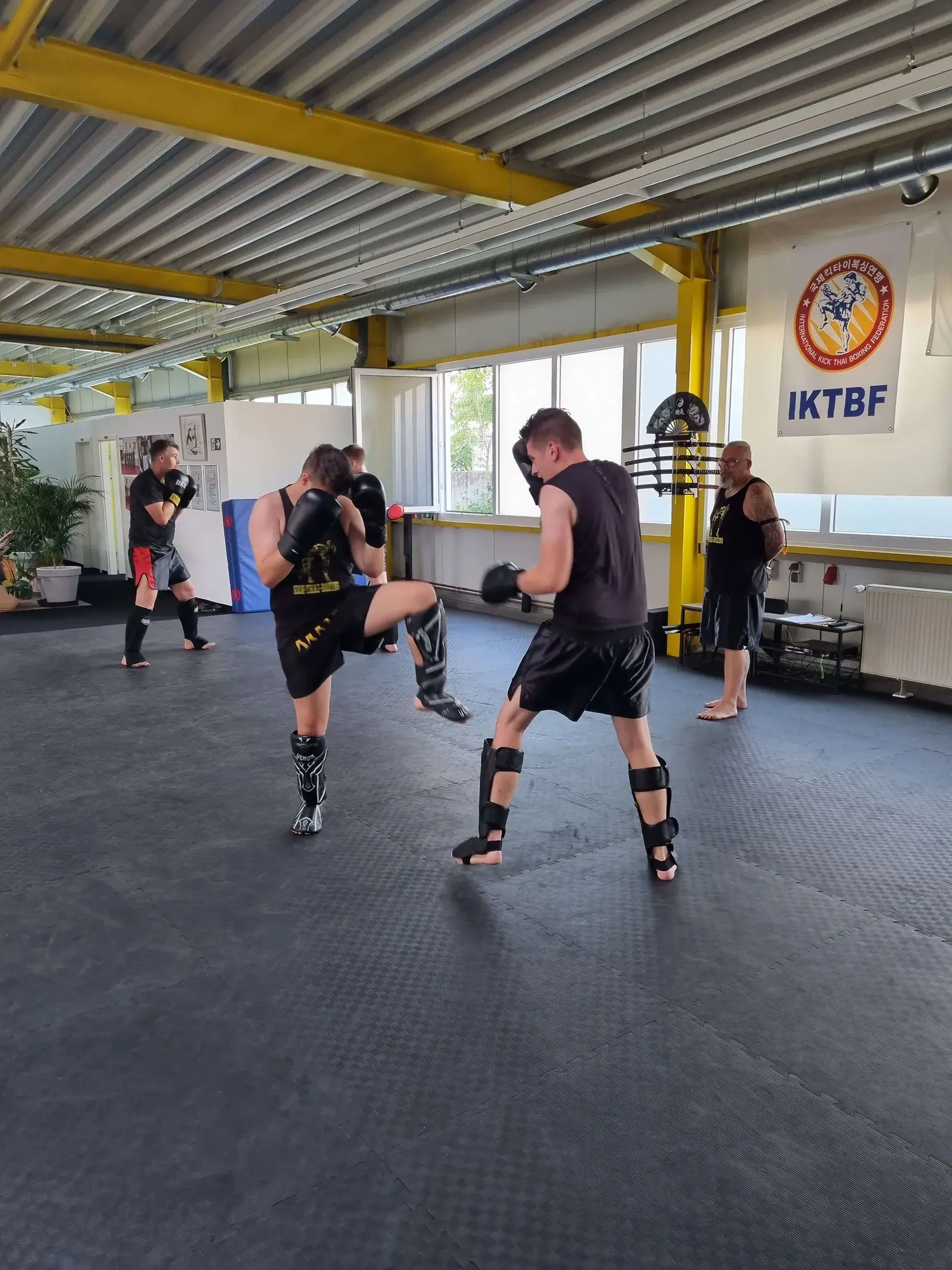 Kampfkunstschule Korean Fighters Werl - Kick-Thai Boxing - Sparring Kick-Thai-Boxing Sparring im Dojang der Korean Fighters Werl: zwei Trainierende mit Schienbeinschonern üben kontrolliert, während im Hintergrund weitere Paare trainieren.