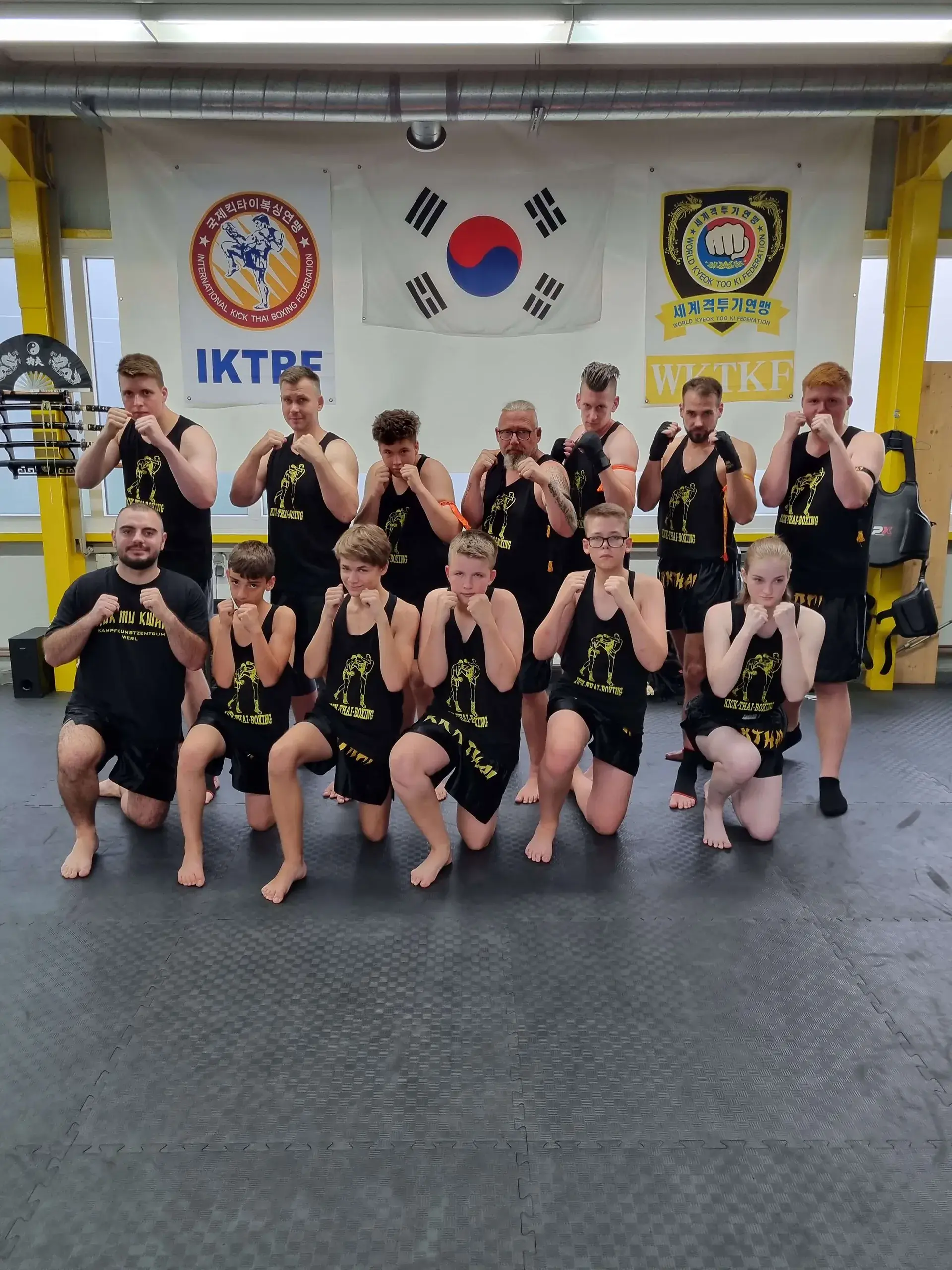 Teamfoto der Kick-Thai-Boxing Gruppe der Korean Fighters Werl: Jugendliche und Erwachsene posieren in Kampfstellung vor Verbandsbannern und der koreanischen Flagge.