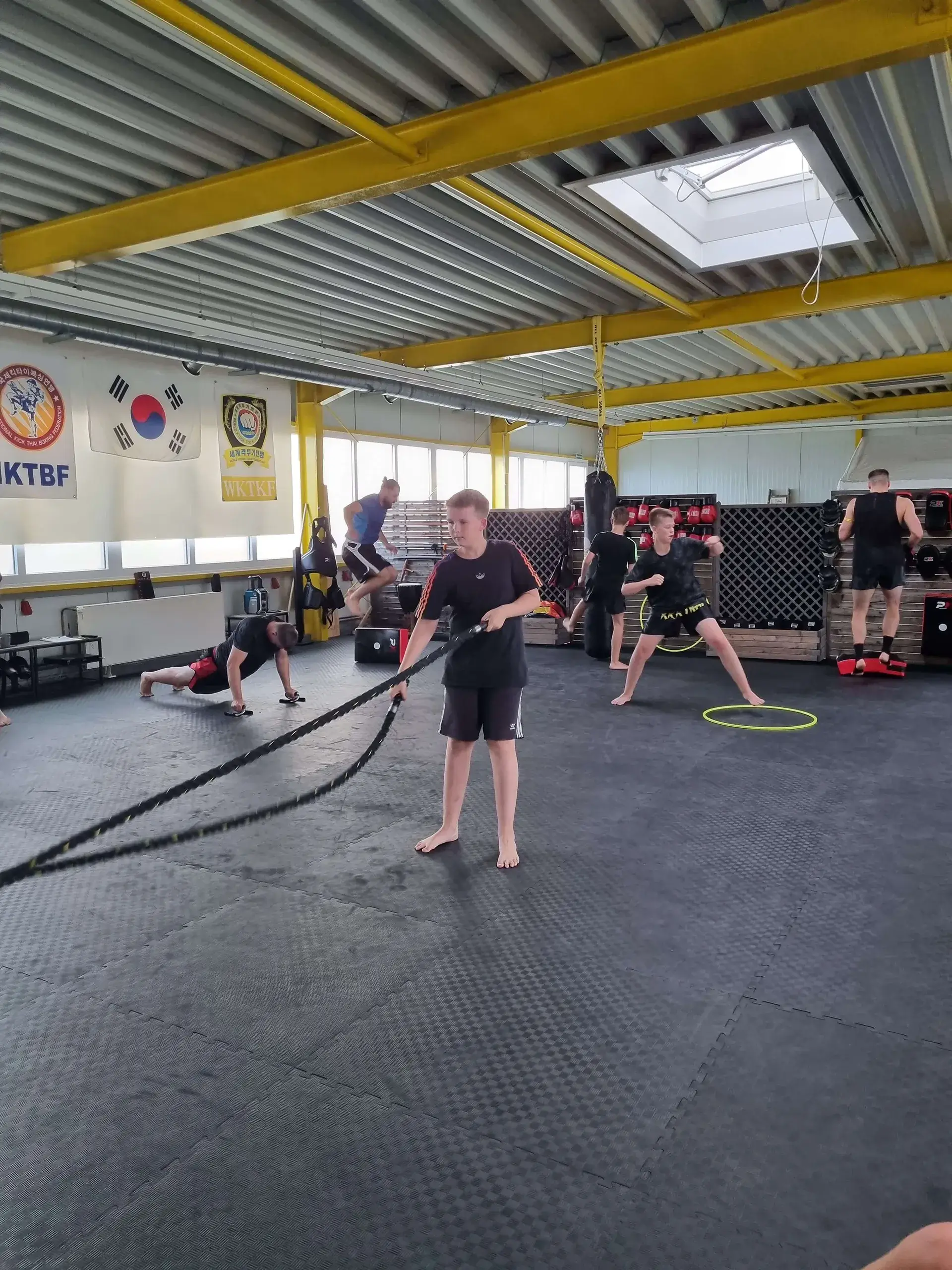Kampfkunstschule Korean Fighters Werl - Kick-Thai Boxing - Zirkeltraining Kick-Thai-Boxing Zirkeltraining bei den Korean Fighters Werl: ein Jugendlicher trainiert mit Battle Ropes, im Hintergrund laufen weitere Stationen wie Kraft- und Technikübungen.