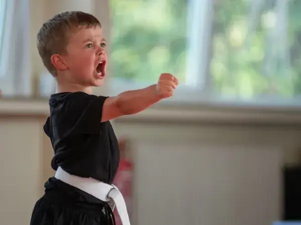 Kampfkunstschule Korean Fighters Werl - Kampfpsort in Werl - Kachel - Kyeok Too Ki Minis Korean Fighters Werl – Kampfsport in Werl: Ein Kind aus den Kyeok Too Ki Minis streckt die Faust nach vorn und ruft laut; Übung für Mut, Stimme, Fokus und Grundtechnik im Training.